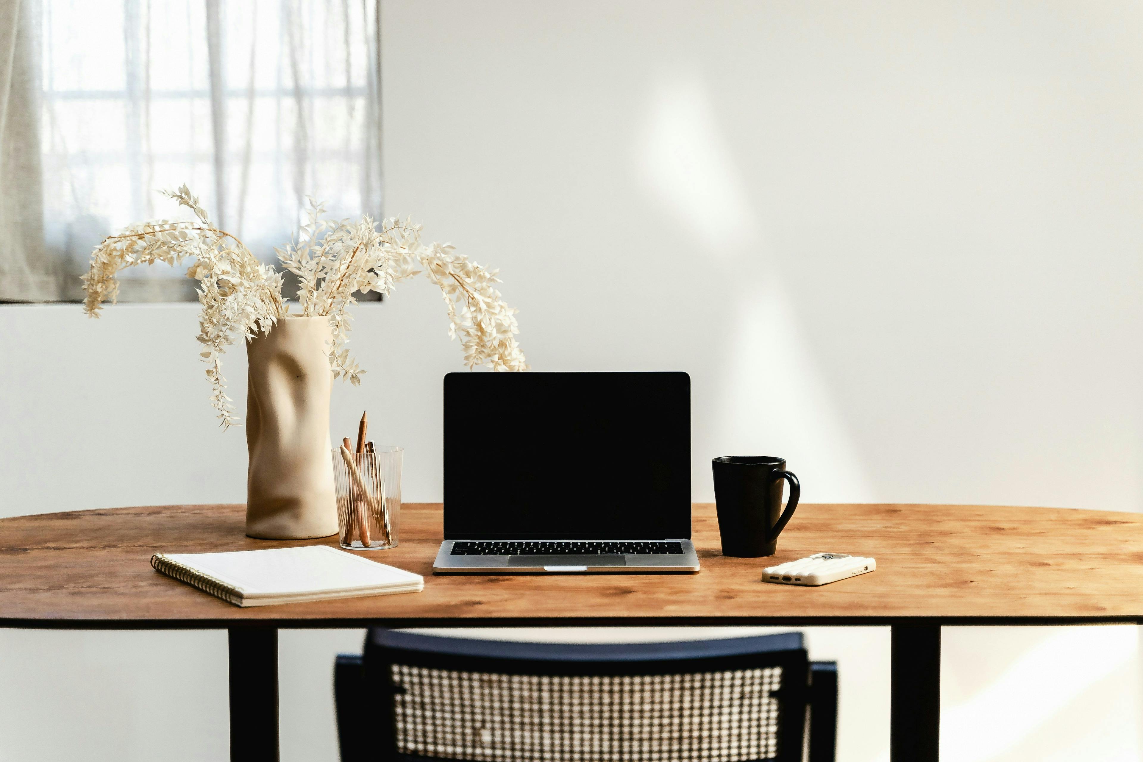 Office table with open computer, notebook and coffee mug